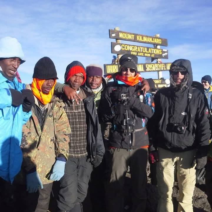Climbers celebrating at the Kilimanjaro summit sign